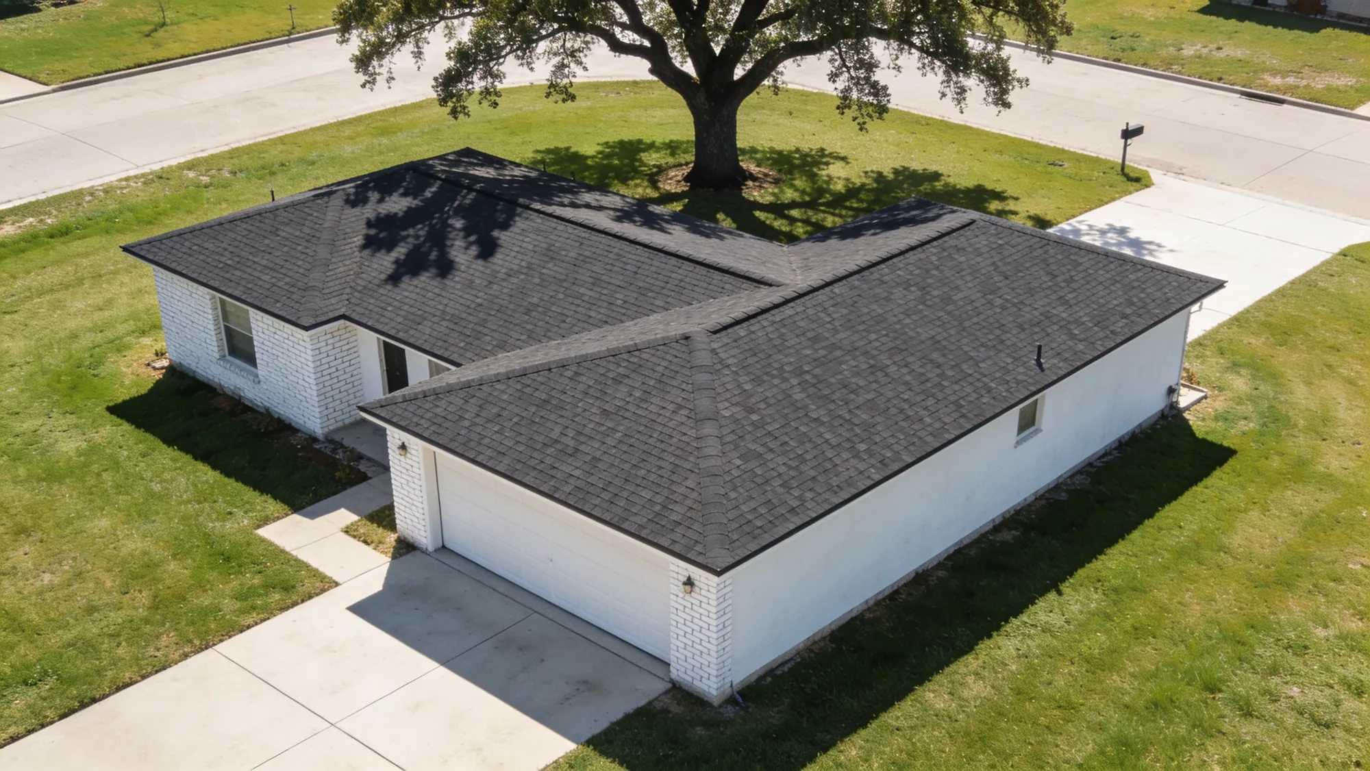 Overhead view of a single-storey house with a clean shingle roof and a mown lawn in bright sun.